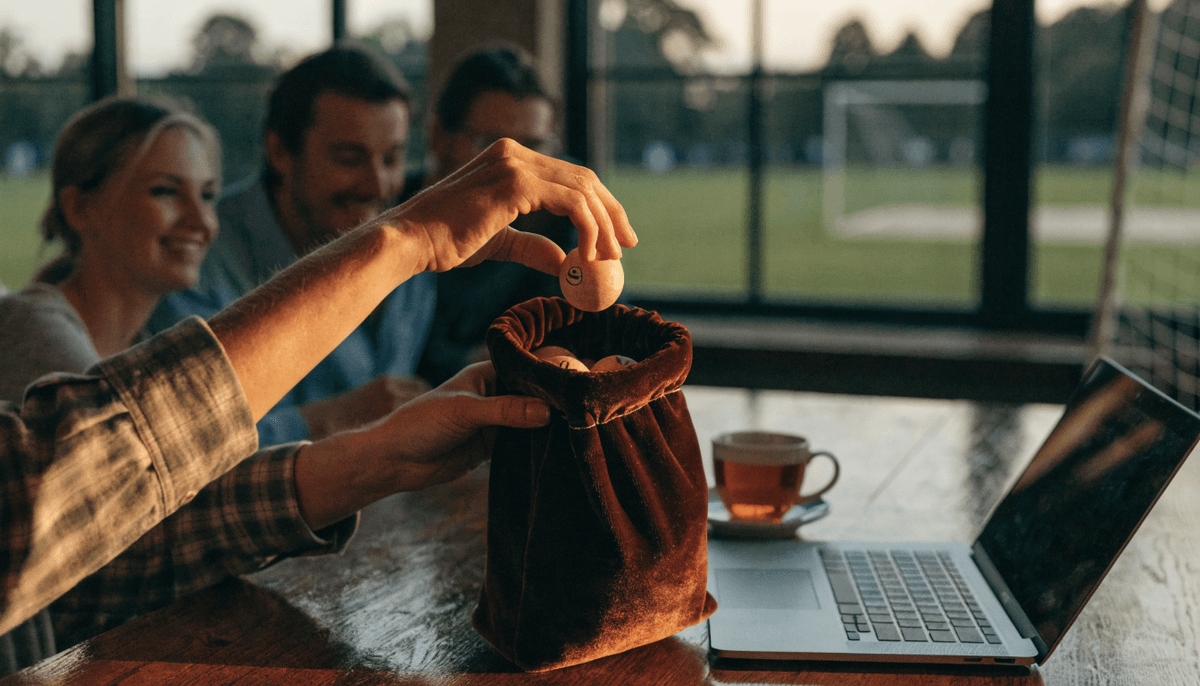 Club volunteer drawing a numbered ball from a bag at a clubhouse table while members watch